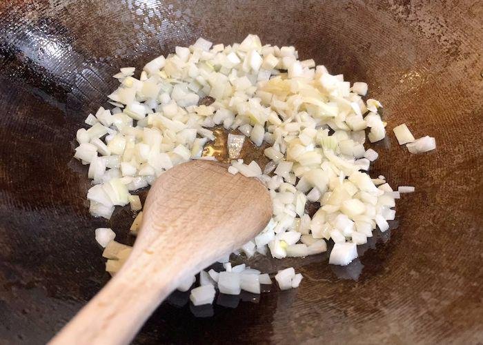 Onions frying in a wok with wooden spoon