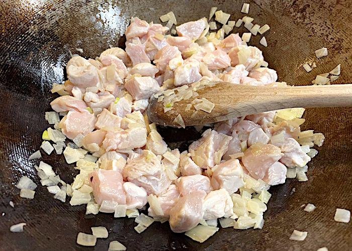 Chicken and onions browning in a wok with wooden spoon