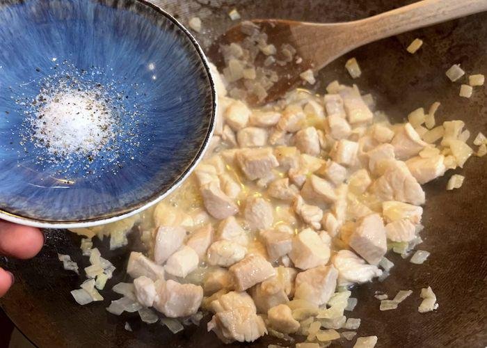 Chicken and onions in wok adding bowl of salt and pepper
