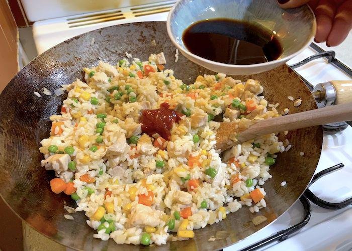 Adding soy sauce to wok with rice mix for Omurice