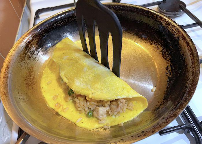 Omelette rice getting folded into omurice in a fryin pan