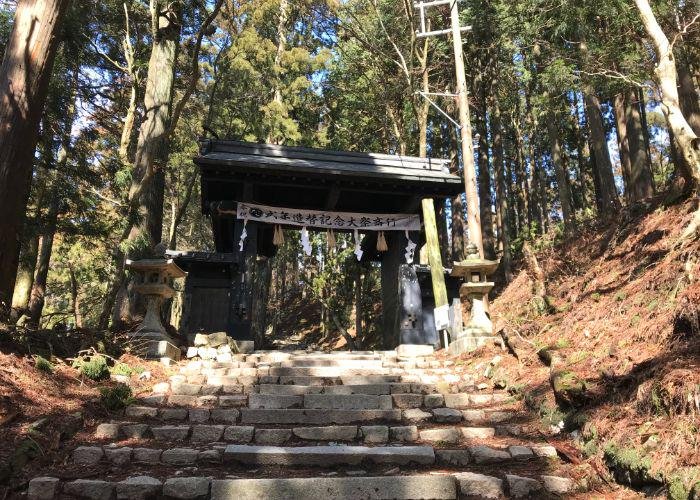 A set of steps leading up the mountainside to a black torii gate on Mount Atago