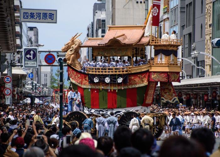 A huge float shaped like a boat with a dragon at the front being pulled through crowded streets during Gion Matsuri festival