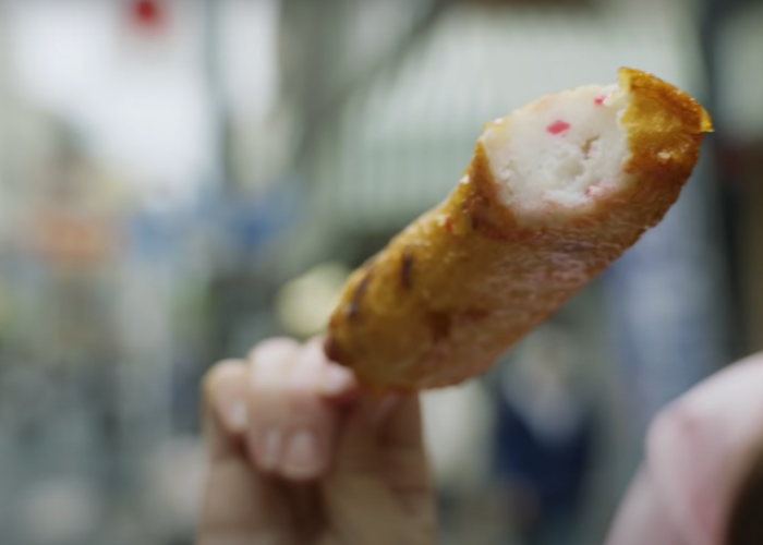 A hand holds out a stick of isoage (fish cake)
