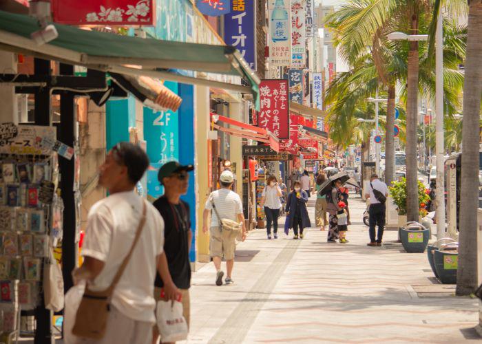 People shopping on a sunny sidewalk lined with palm trees