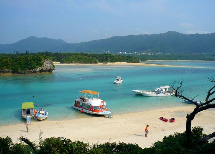 A view of four boats in Kabira Bay on Ishigaki Island, with a golden sandy beach in the foreground and emerald waters behind