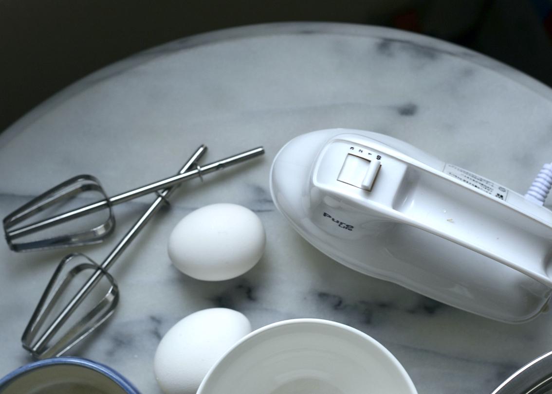 Hand mixer, bowls, and eggs laid out on a marble tabletop