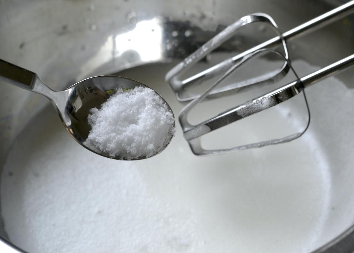 Spoonful of granulated sugar in front of a bowl of frothy egg whites