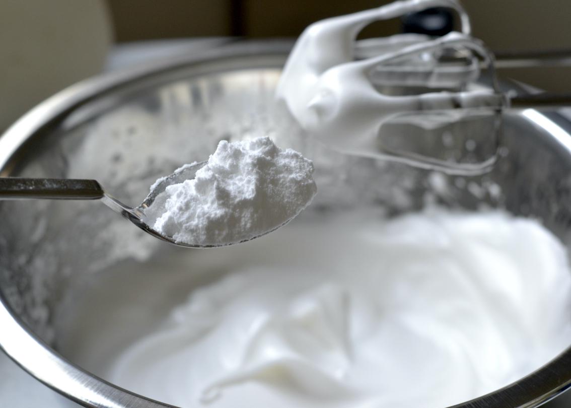 Spoonful of powdered sugar being added to a bowl of meringue