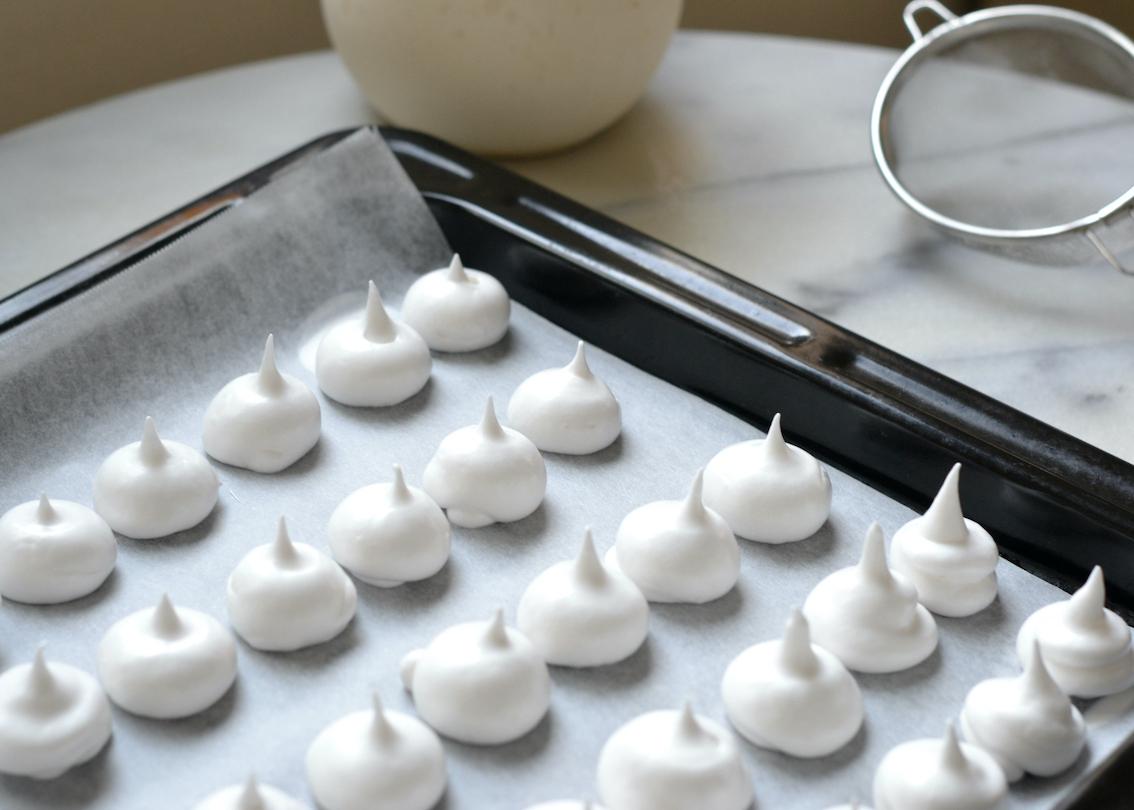 Kiss-shaped piped meringues on a baking tray