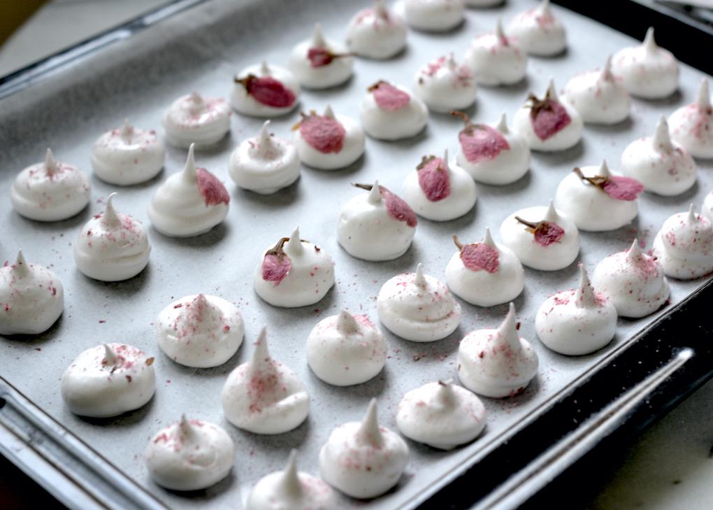 Piped meringues decorated with cherry blossoms and freeze-dried sakura on a baking tray 