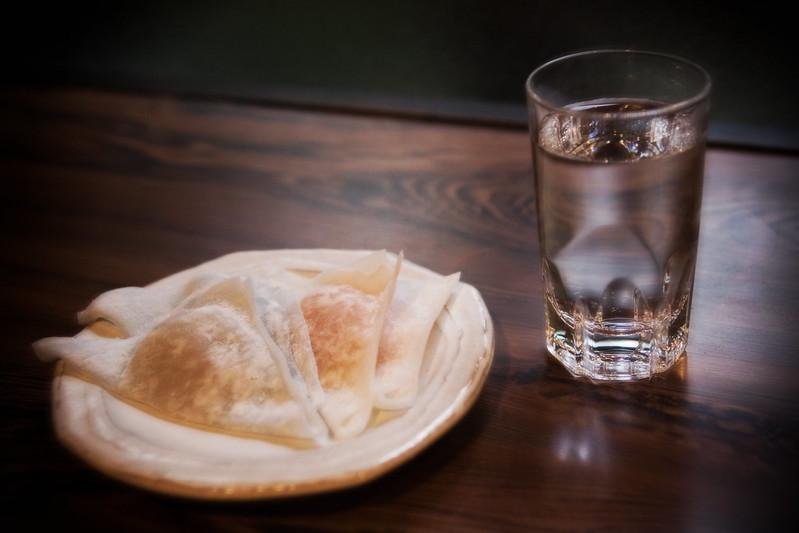 Yatsuhashi on a plate next to a glass of clear sake