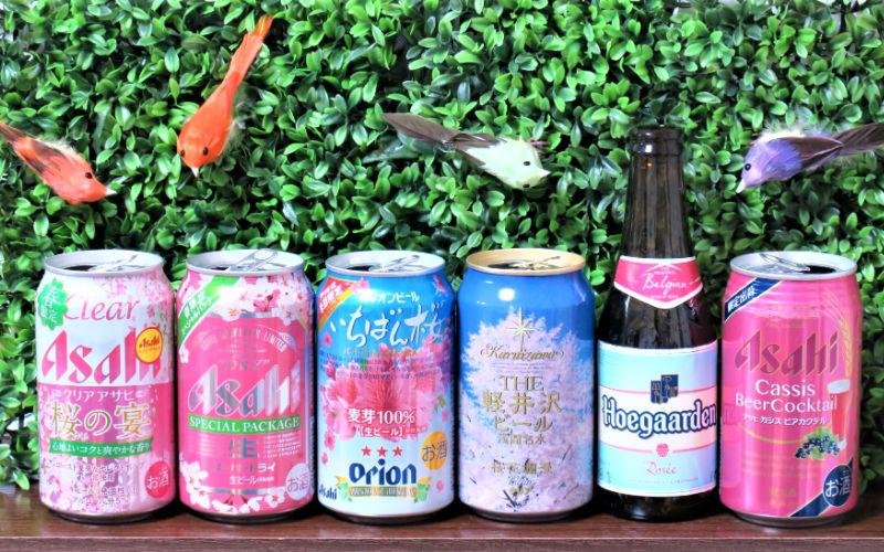 Different sakura spring themed Japanese beers in a row in front of a green background with birds