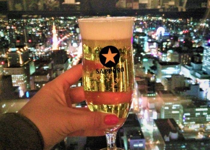 Glass of Sapporo Beer in front of a night window looking out onto Sapporo cityscape