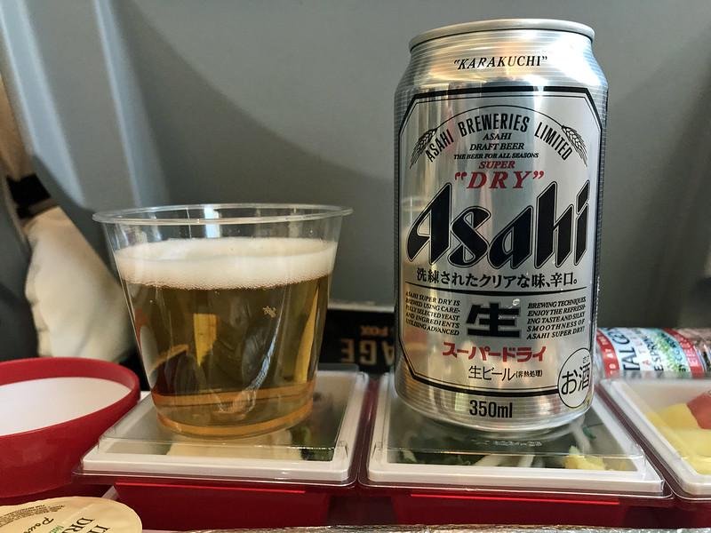Plastic cup with beer next to Asahi Super Dry can on a shinkansen bullet train tray