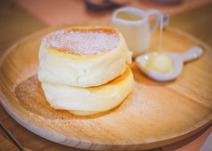 Stack of fluffy pancakes on wooden plate with powdered sugar and a small jug of maple syrup 