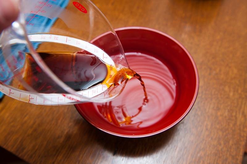 Pouring dashi into a lacquer cup on a wooden table
