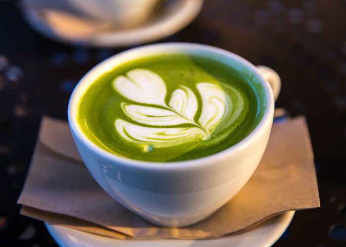 A cup of matcha latte on a saucer, with a green and white artistic pattern on top