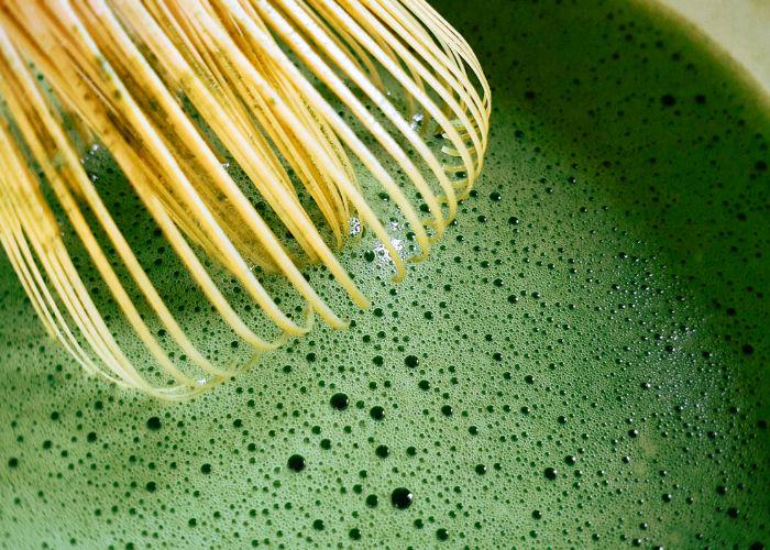 A close up image of a bamboo chasen in a frothy bowl of matcha