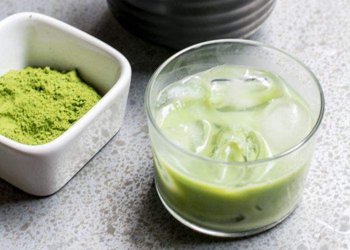 A white bowl full of green matcha powder next to a glass of iced matcha latte