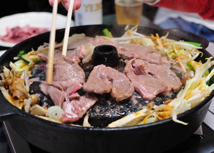 Close-up of "jingisukan" mutton BBQ, featuring slices of mutton, beansprouts and onions on a hot grill.