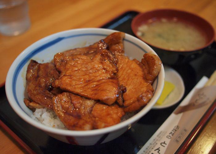 A table with a bowl of soy-glazed pork over rice.