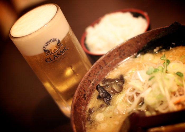 A glass of Sapporo beer behind a bowl of Sapporo ramen noodles.