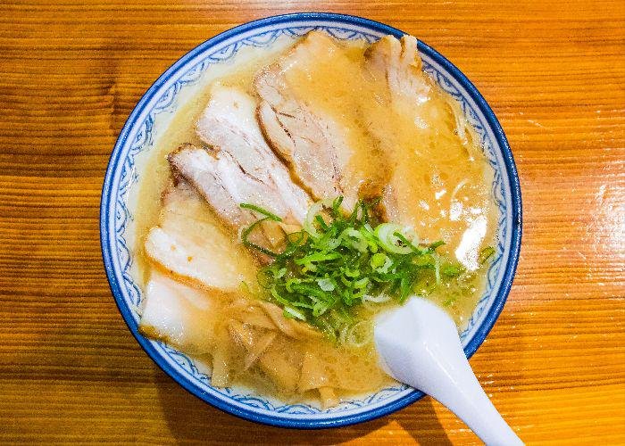 A bowl of ramen noodles with tonkotsu broth, chashu and onions