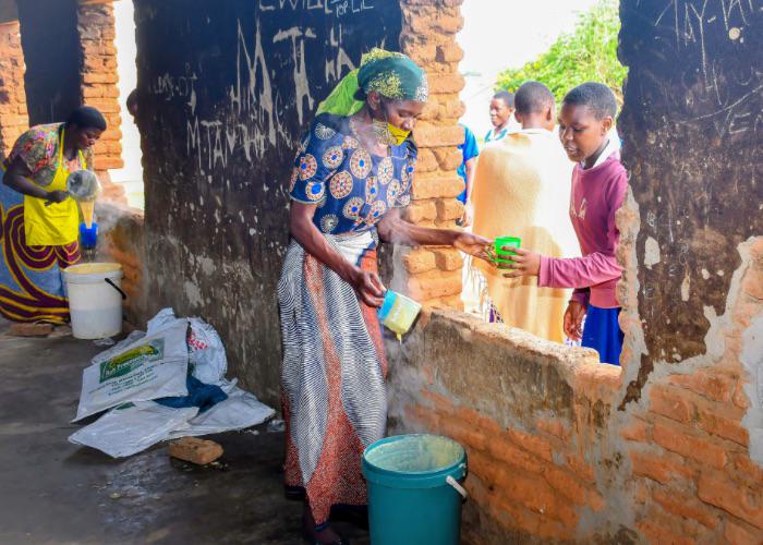 two volunteer or staff members are pouring flour porridge into students' meal containers