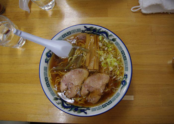 Overhead image of a bowl of noodles with two big slices of meat, bamboo shoots and green onions