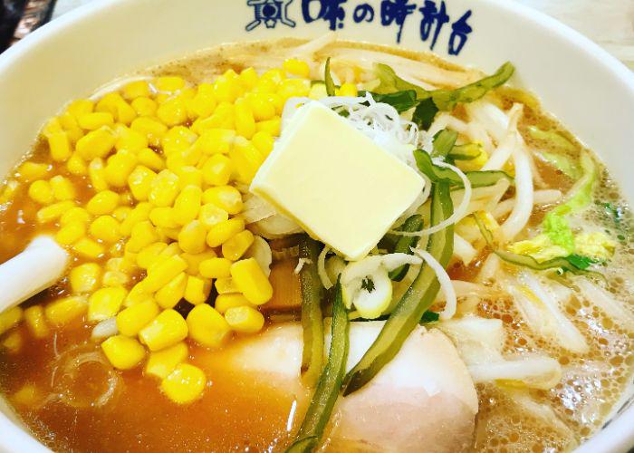 A close-up shot of a bowl of ramen with lots of bright yellow sweetcorn and a pat of butter in the center