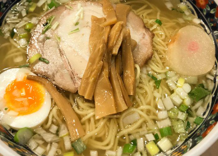 A very close-up picture of a bowl of ramen topped with half an egg, bamboo shoots, green onions and a slice of meat