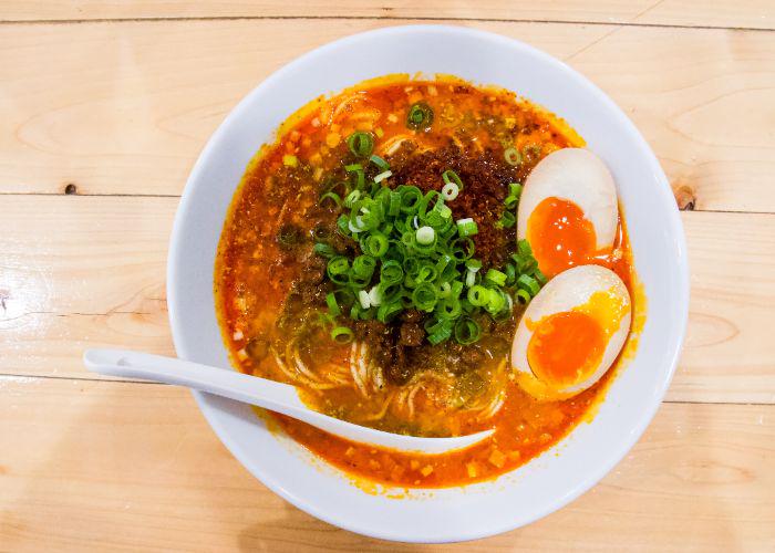 Overhead shot of a bowl of ramen with a vibrant red broth, topped with two halves of an egg and a pile of sliced spring onions