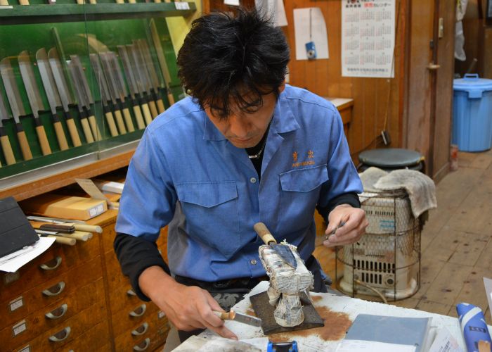 Japanese man in a blue shirt working on a knife in a knife shop