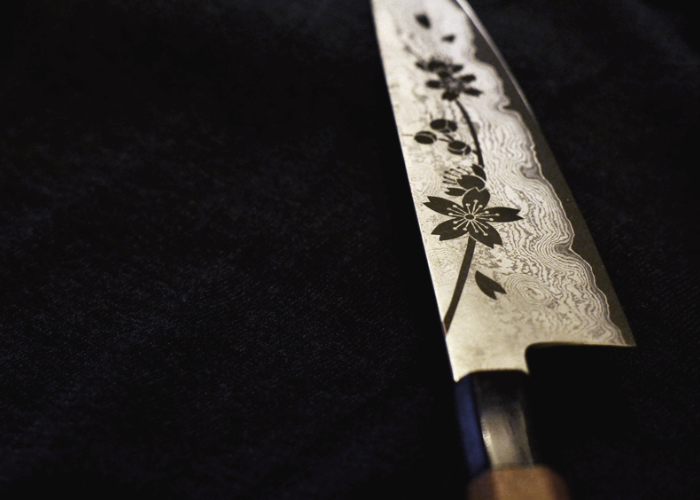Close up image of a Japanese knife on a black background, with a sakura design on the blade