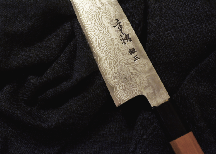 Close up of a Japanese knife on a black background with kanji on the blade