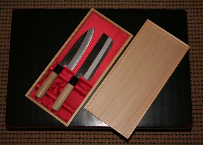 Overhead image of an open wooden box containing two Japanese knives on a red cloth