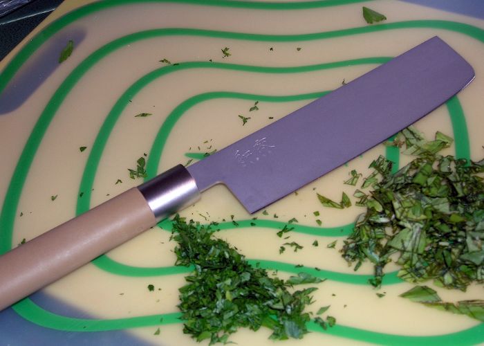 Overhead image of a rectangular knife on a white and green chopping board, surrounded by finely cut leaves
