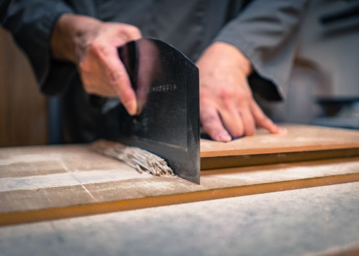 Close up image of a person using a menkiri knife to cut a strip of soba noodles on a wooden board
