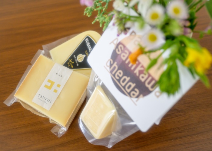 A group of cheeses on a table under a vase of flowers.