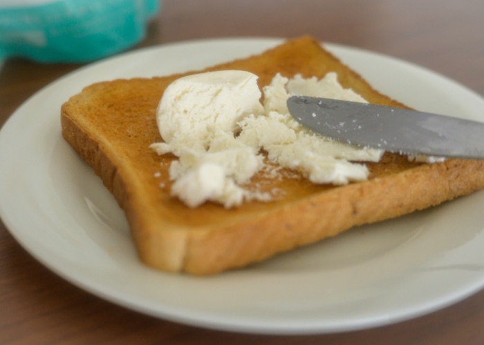 A knife spreading ricotta cheese over a slice of toast.