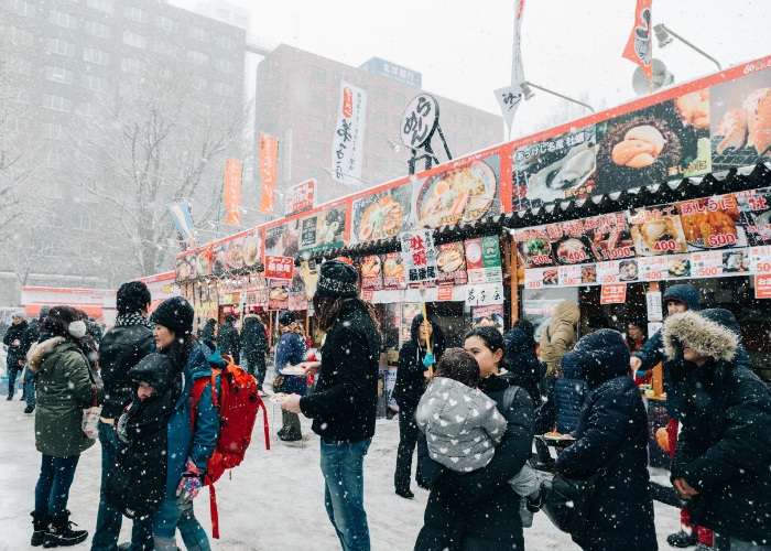 Food stalls at Sapporo Yuki Matsuri Snow Festival with people queuing up in the snow
