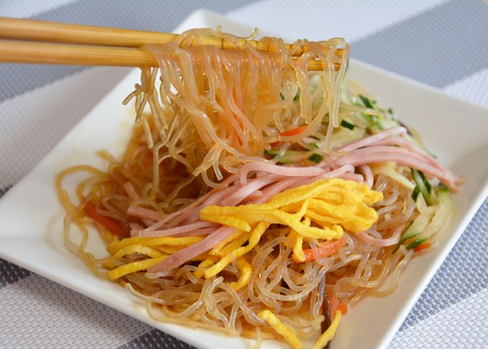 Chopsticks lifting translucent harusame noodles from a white plate