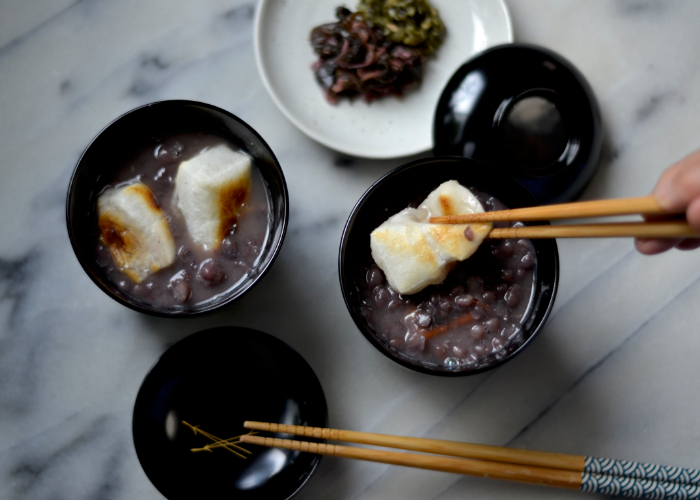 Chopsticks raising toasted mochi from a bowl of zenzai, Japanese sweet bean soup