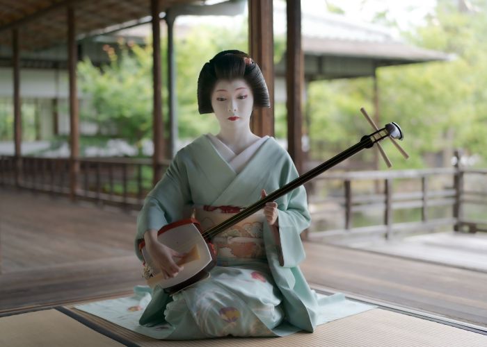 An image of a geisha in a light green kimono playing a shamisen