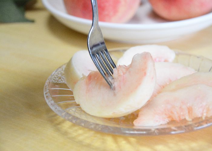 A plate of juicy Japanese white peach slices, one being picked up with a fork