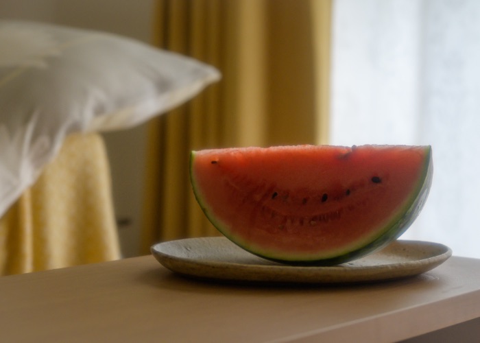 A slice of watermelon on a plate beside a window.