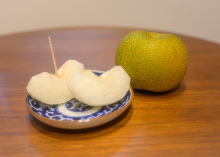 A whole Nashi pear next to a plate of slices of Nashi pear.