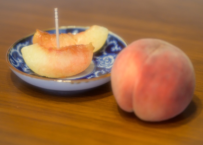 A whole peach next to a plate of peach slices.
