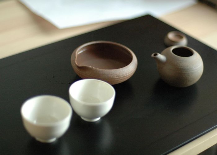 A small brown teapot and two white teacups on a black board